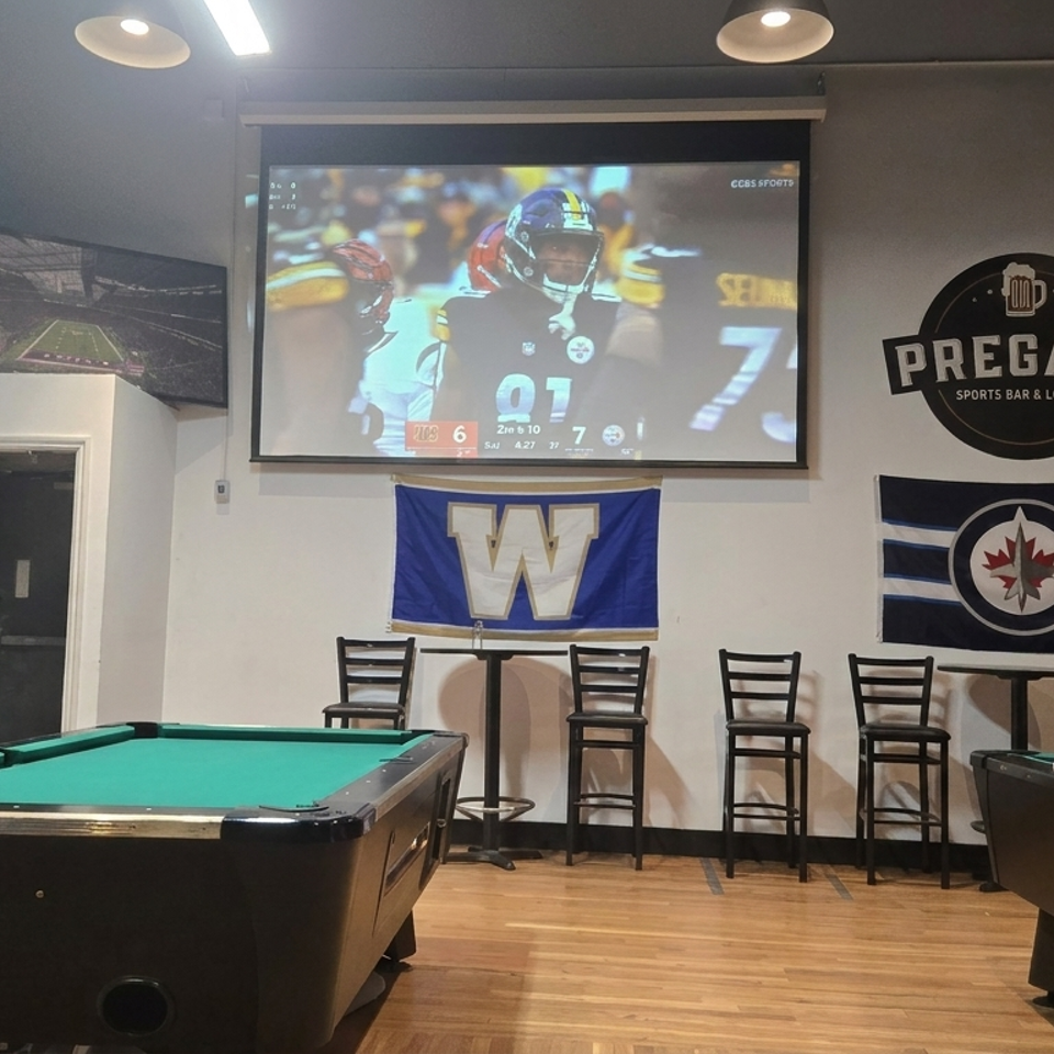 Sports bar lounge with two pool tables, bar seating, sports memorabilia, and a football game playing on a large screen.